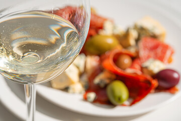 Poster - cool white wine in a glass near a plate with sliced ham, dove cheese and various olives