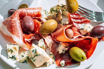 Wall Mural - cool white wine in a glass near a plate with sliced jamon, dove cheese and various olives. a light snack on a hot day. classic italian food.