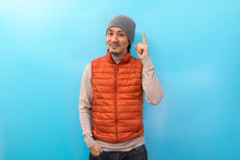 Winter Fashion. Handsome Asian Man With Hat And Orange Jacket Pointing Finger Over White Isolated Background.