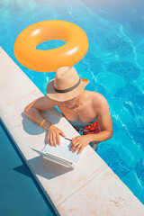 Man in hat by the swimming pool surfing internet through his laptop or notebook pc. Studying at online university and remote work. Freelancing as a dream job concept