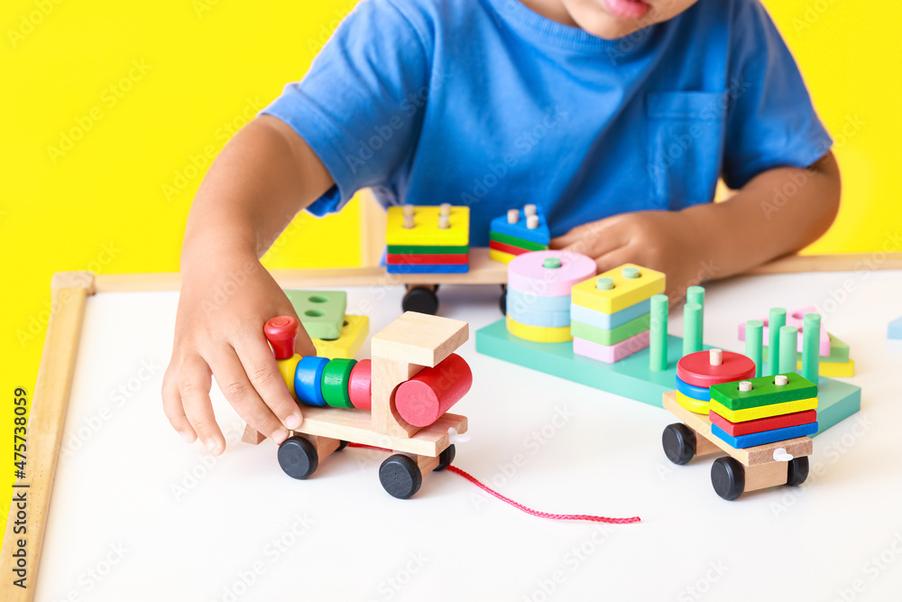 Little boy playing with building blocks at table on yellow background, closeup