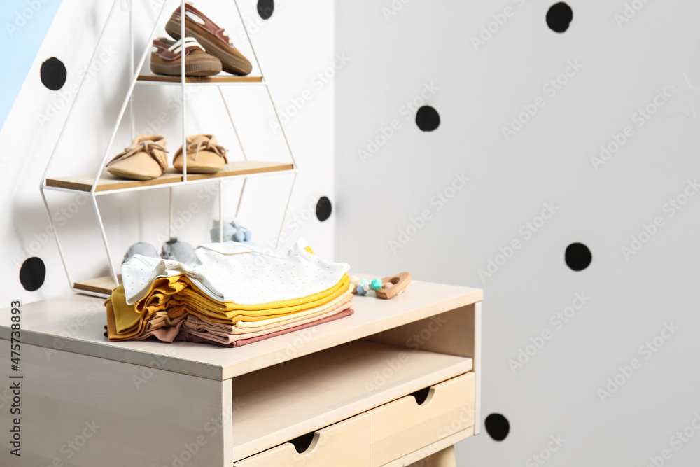 Stand-up table with baby clothes near color wall