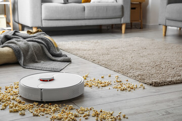 Modern robot vacuum cleaner with scattered popcorn on floor in room