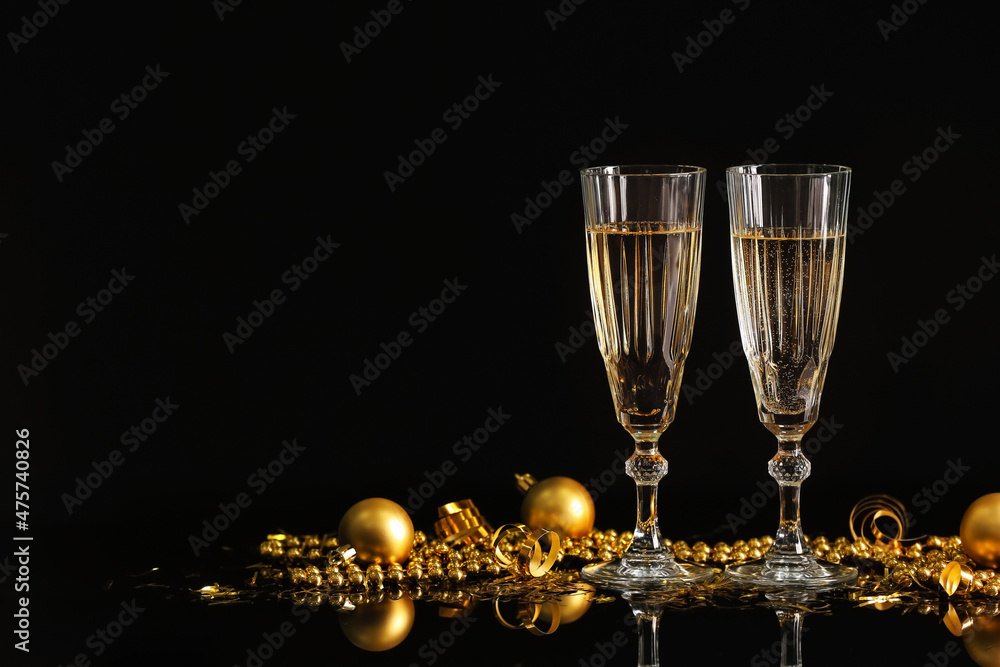 Glasses with champagne and Christmas decorations on black background