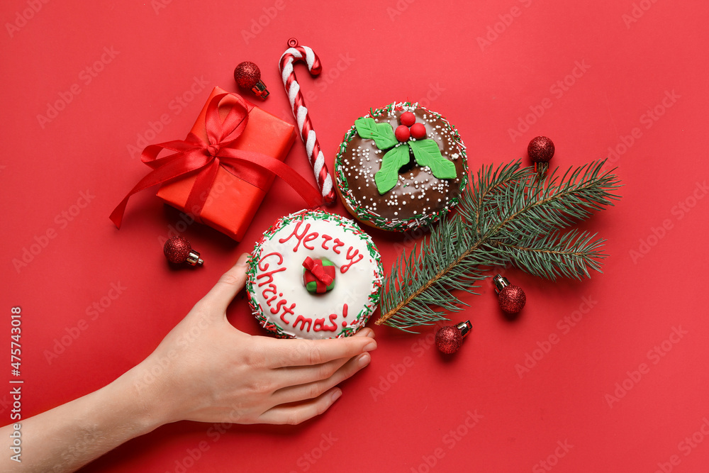 Female hand with tasty Christmas donuts and decor on red background