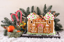 Board With Beautiful Gingerbread House, Tangerines, Snow And Treats On White Wooden Background