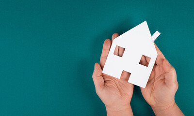 Holding a small paper house in the hands, planning to buy or rent a new home, real estate, owning property