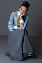 A Working Class Edwardian Woman Wearing A Striped Blouse, Mustard Yellow Cravat, And Walking Skirt And Sitting Alone