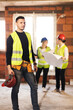 © Nikola Spasenoski - male worker on a residential construction site with his team of engineers working in the background