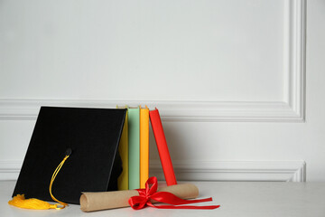 Wall Mural - Graduation hat, books and diploma on floor near white wall, space for text