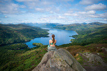 Scenic Shot Of A Woman From Her Back Sitting On A Rock On The Muntain Looking At The Calm Lak