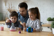 Caring father with little kids playing with toy laboratory, engaged in interesting educational activity, Caucasian young dad and children making experiments, spending leisure time at home together