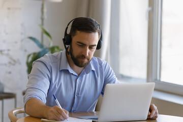 focused young man in headset with microphone listening educational lecture on computer, studying on 