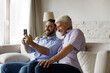 © fizkes - Happy two male generations family using cellphone, posing for funny selfie photo, recording video or holding web camera call conversation together at home. modern tech gadget usage addiction concept.