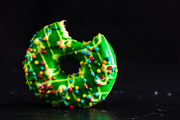 Sticker - Closeup shot of a green bitten donut with colorful sprinkles isolated on a black background