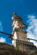 Blick von unten auf eine weibliche Statue, die auf einem Sockel steht, vor strahlend blauen Himmel