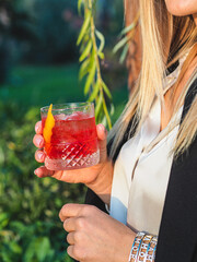 Poster - Vertical closeup of the woman's hand holding a pomegranate rosemary gin cocktail.