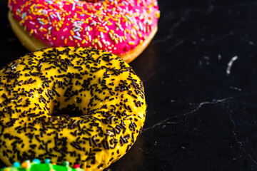 Wall Mural - Closeup shot of pink, yellow and green glazed donuts with sprinkles isolated on a black background