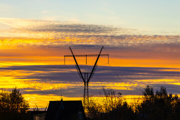 Black power line is on the blue sky background with pink and orange and yellow clouds at the sunset