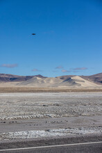 Portrait Of Tiny Black Drone Flying Away Towards Sand Dunes Of Sand Mountain OHV Park
