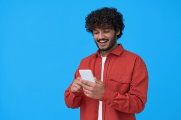 Happy indian young man using cell phone isolated on blue background. Smiling guy holding smartphone texting on mobile in social media network chats communication platform technology.
