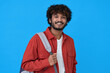 © insta_photos - Smiling young curly bearded indian cool positive guy holding backpack standing isolated on blue background. Happy ethnic man university student with bag advertising education course, portrait.