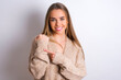 © Roquillo - young caucasian girl wearing knitted sweater over white background In hurry pointing to wrist watch, impatience, looking at the camera with relaxed expression