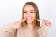 © Roquillo - young caucasian girl wearing knitted sweater over white background holding an invisible aligner and pointing to her perfect straight teeth. Dental healthcare and confidence concept.