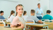 Portrait of positive teenage schoolgirl sitting at lesson in classroom, looking confidently at camera..