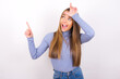 Young caucasian girl wearing blue turtleneck over white background showing loser sign and pointing at empty space
