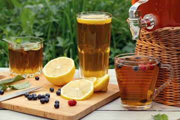 Wall Mural - Homemade mushroom kombucha drink in a jar with a tap and in glasses with mint, berries and lemon on a wooden table