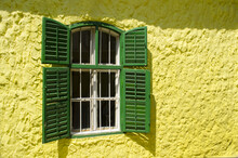 Old Wooden Window With Metal Bars And Green Shutters On A Yellow Wall In Dobrica, Banat, Serbia