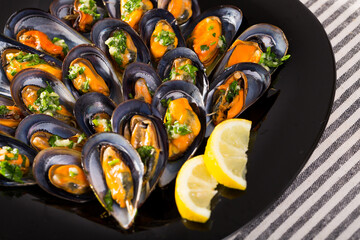 Wall Mural - Gourmet steamed mussels with garlic herb sauce served on black dish with lemon..