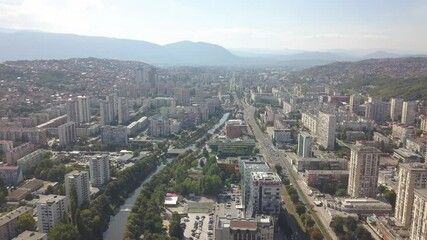 Sticker - A beautiful view of a city with high buildings among hills, with a small river running in the middle