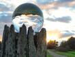 Glass ball on a rotten trunk reflecting a landscape and the cloudy sky during sunset