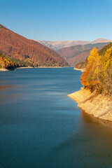 Beautiful view of a lake with hill in the background covered by trees in autumn colors in Romania