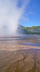 Sticker - Vertical shot of a pond with steam on the background of hills and trees under a blue sky in winter