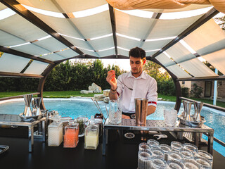 Poster - Young Caucasian barman making a refreshing cocktail outdoors by the pool at an event