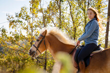 Young Woman Horseback Riding By Trees