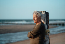 Senior Man Leaning On Wooden Post At Beach