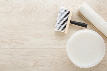 Roll of wallpaper, brush, bucket with glue on light wooden table background. Closeup. Preparation for repair work of home. Empty place for text. Top down view.