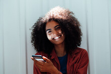 Smiling Woman With Smart Phone Leaning On White Wall