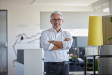 Smiling Businessman Standing With Arms Crossed At Workplace