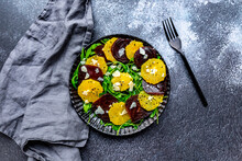 Studio Shot Of Plate Of Vegetarian Salad With Orange And Beetroot Slices, Arugula, Parmesan And Black Sesame Seeds