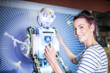 Smiling engineer with screwdriver near human robot in workshop