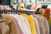 Fashion Faux Fur Coats Hanging On Rack In Clothing Store, Various Colors, Blurred Interior, Girls, Customers