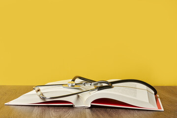 Sticker - Closeup shot of a book and a stethoscope on a wooden table on a yellow background