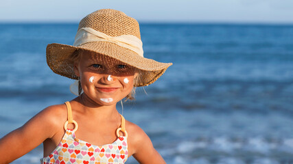 Child sea vacation. Little girl in straw hat with sunscreen on her face on sea background.