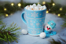 Winter Mug With Marshmellow And Knitted Handmade Stand Snowman In Scarf Against Background Of Festive Lights Bokeh And Fir Branches