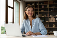 Cheerful Young Female Worker Sitting At Workplace With Laptop In Office, Looking Away, Smiling, Laughing. Millennial Employee, Business Woman In Casual Distracting From Work, Talking To Colleagues